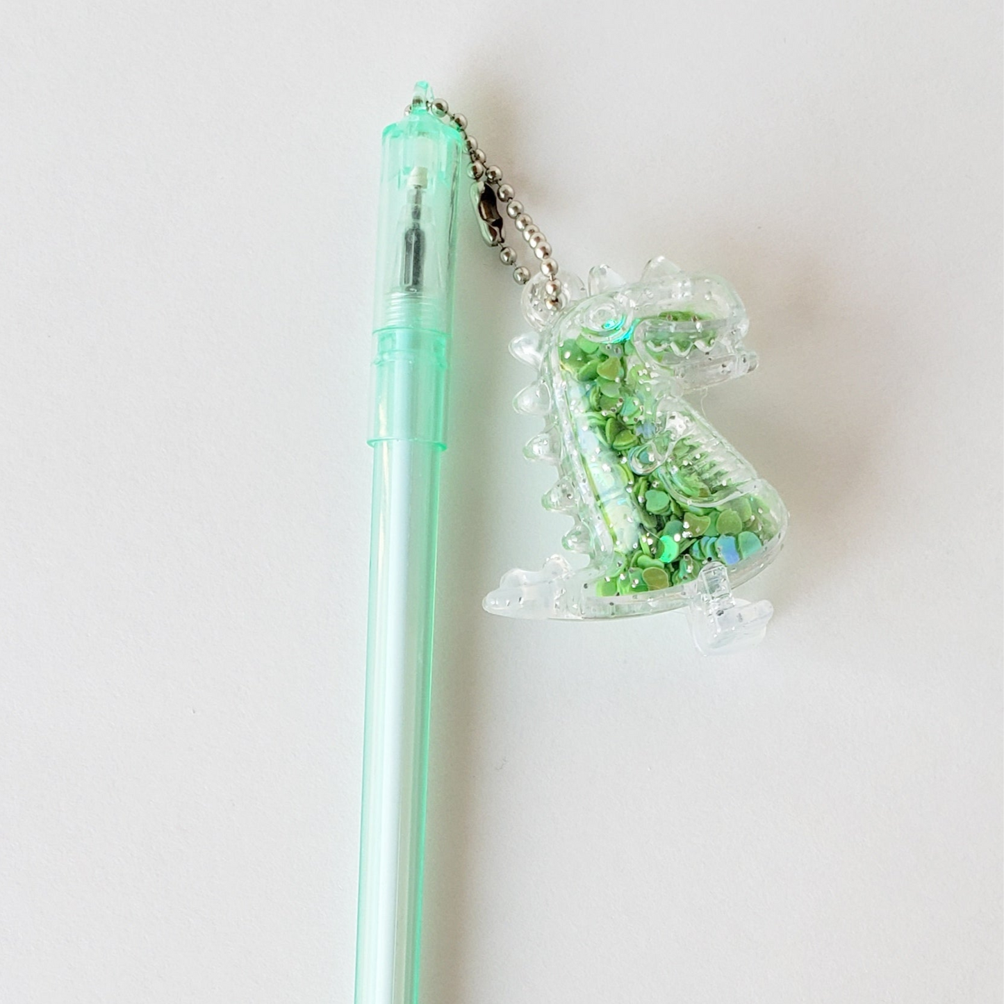 Closeup of the Dino Charm Gel Pen showing the detailed shaker dinosaur charm and ergonomic mint-green barrel grip against a white background
