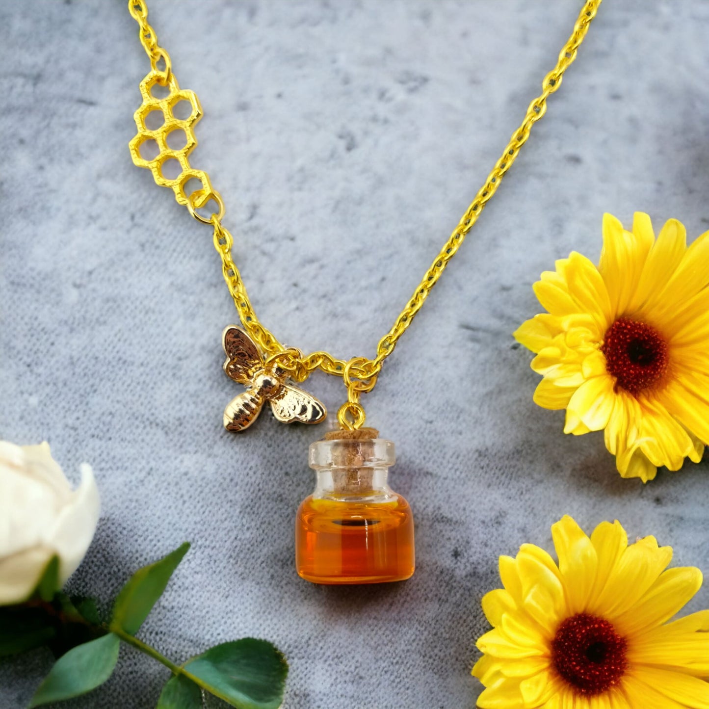 Honey jar necklace with golden bee charm and honeycomb design on gold chain, flowers shown as background only