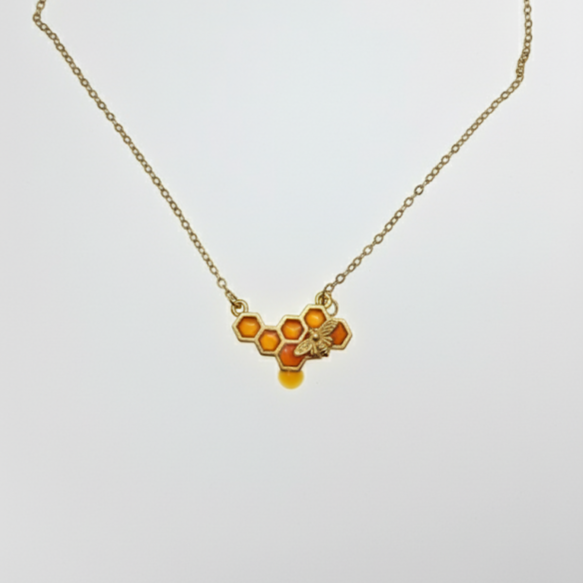 Honeycomb bee necklace with amber enamel detail on gold chain, white background