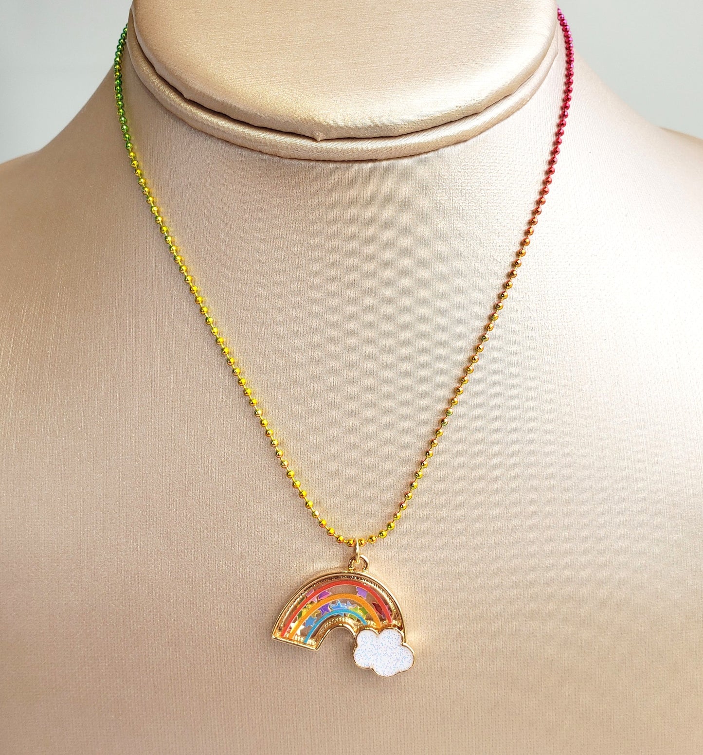 rainbow shaker necklace displayed on a beige jewelry bust showing the rainbow bead chain and confetti-filled pendant