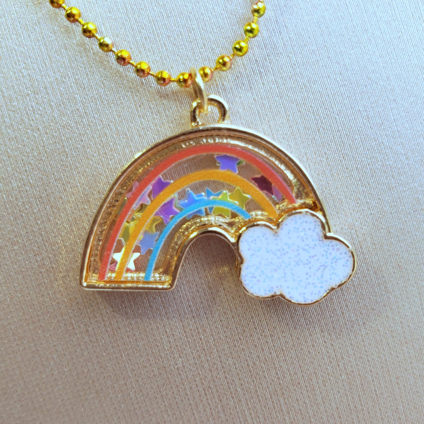 close-up of rainbow shaker necklace pendant filled with star confetti on a gold textured background