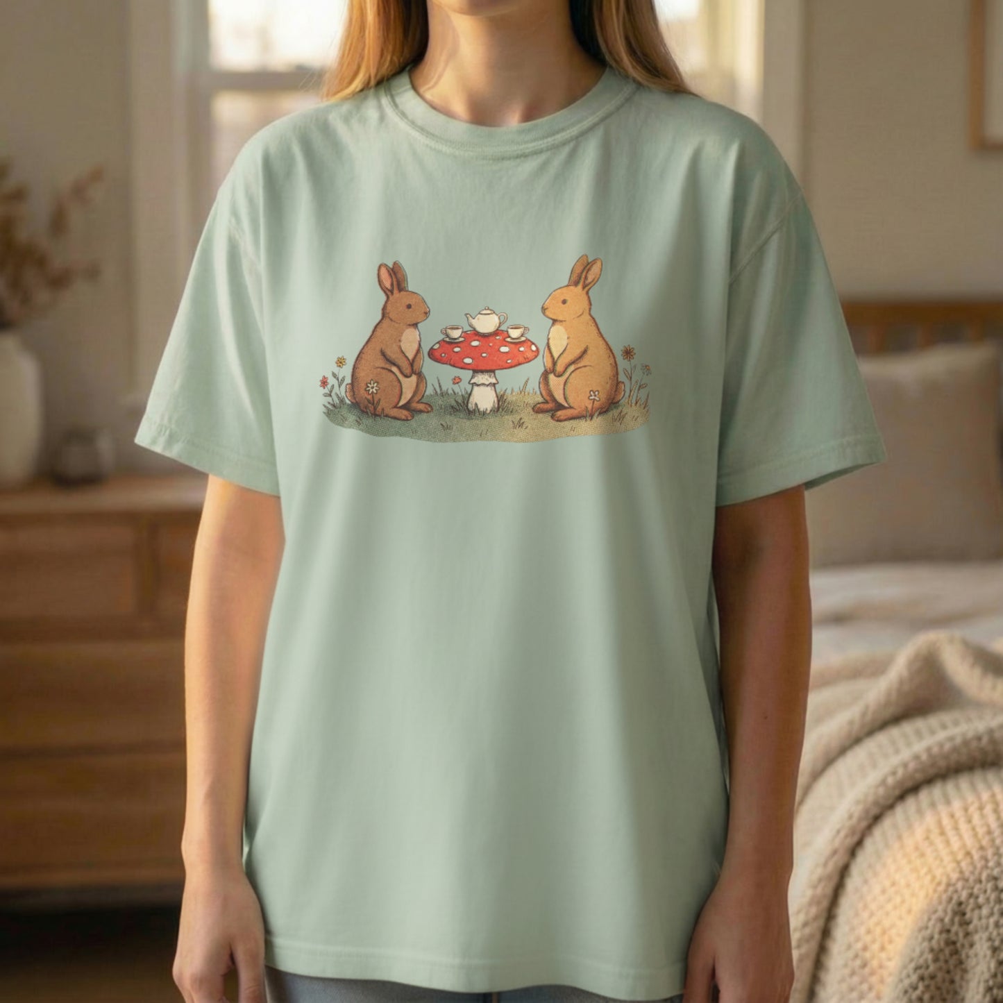 Bunny Picnic Tee worn standing on light green shirt with whimsical rabbit picnic illustration centered on chest