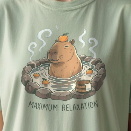 Close-up of a cozy capybara soaking in a hot spring with oranges, printed on a soft cottagecore t-shirt with the text “Maximum Relaxation”.