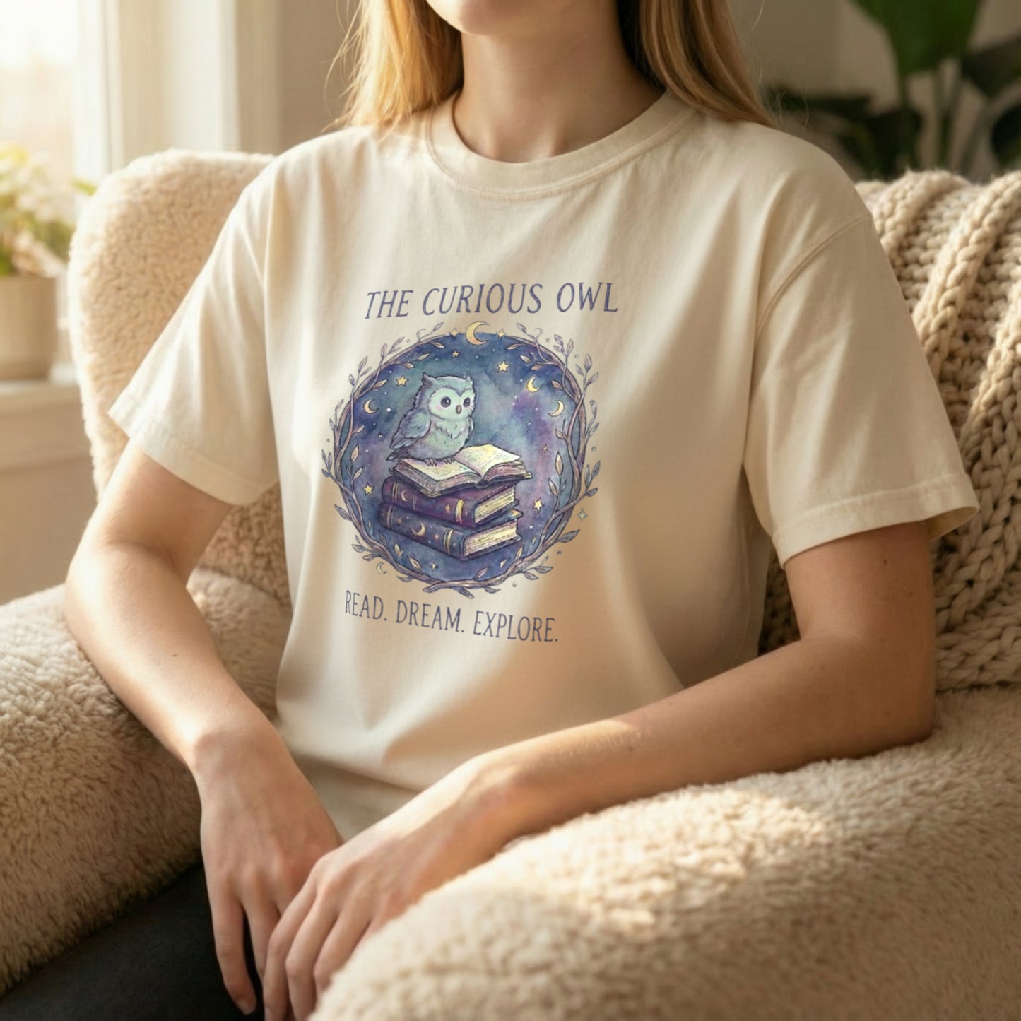 Lifestyle photo of a model seated wearing the Curious Owl tee in ivory with the dreamy owl and book artwork