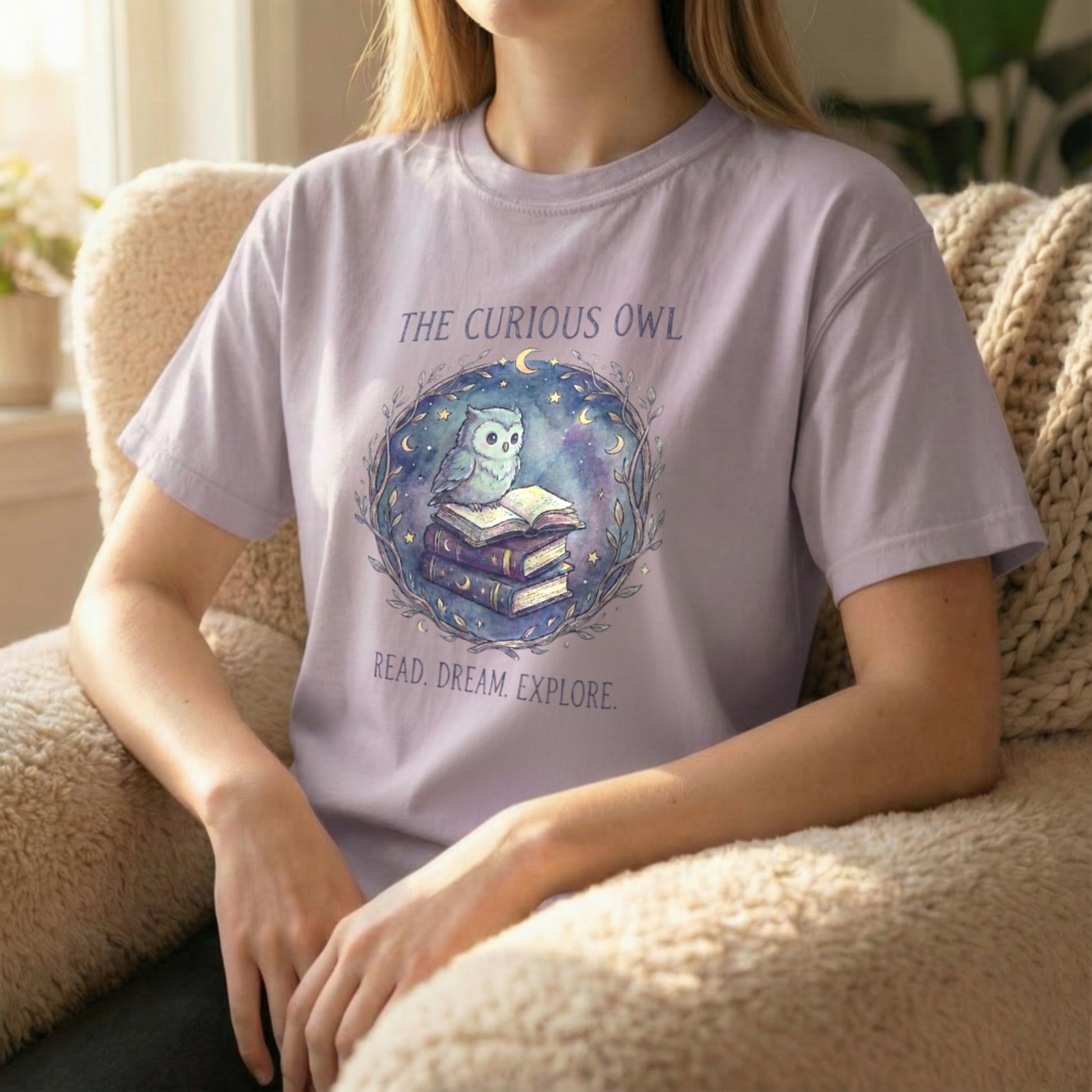 Lifestyle photo of a model seated wearing the Curious Owl tee in orchid, featuring the whimsical owl and book illustration