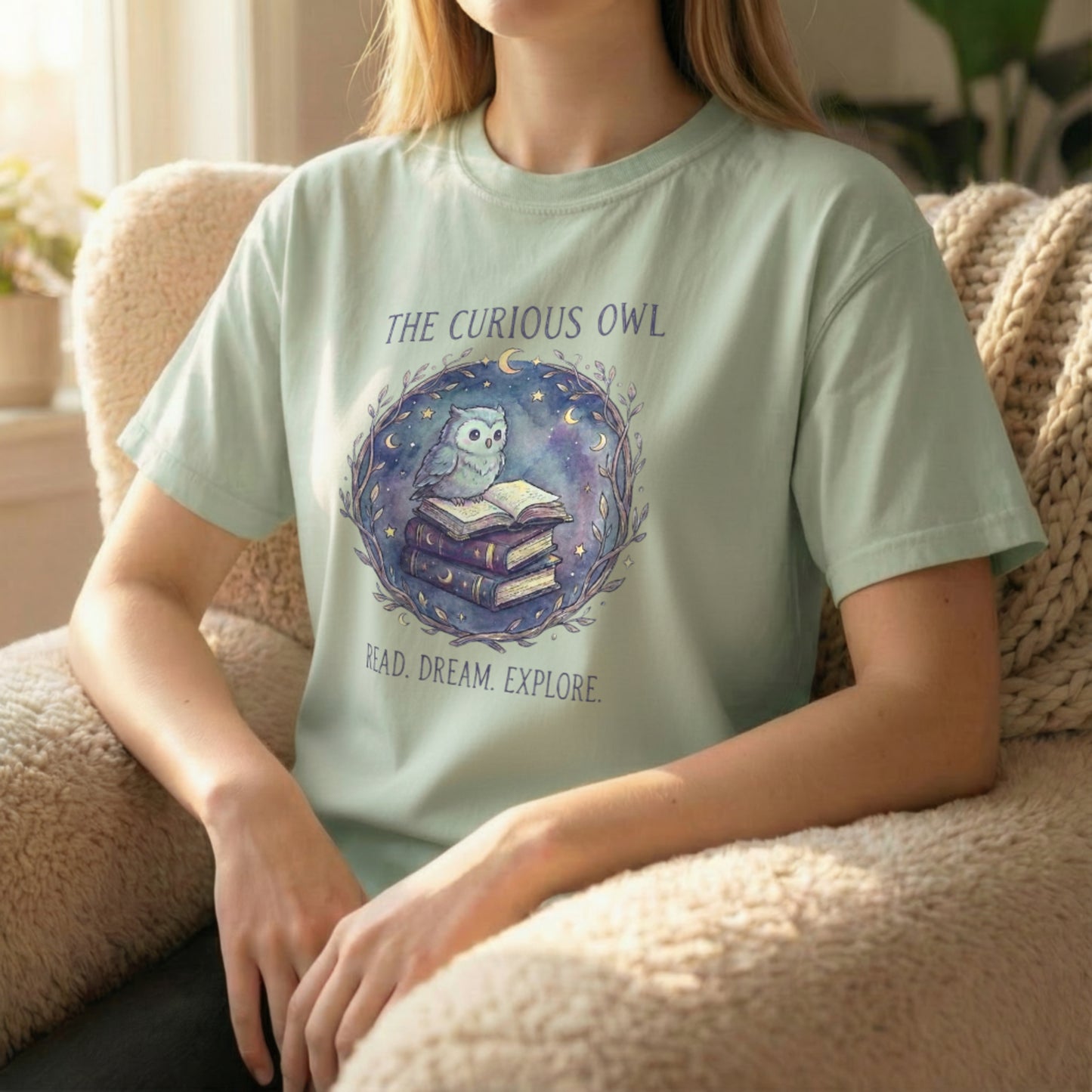 Lifestyle image of a model seated wearing the Curious Owl tee in sage, highlighting the soft watercolor owl artwork