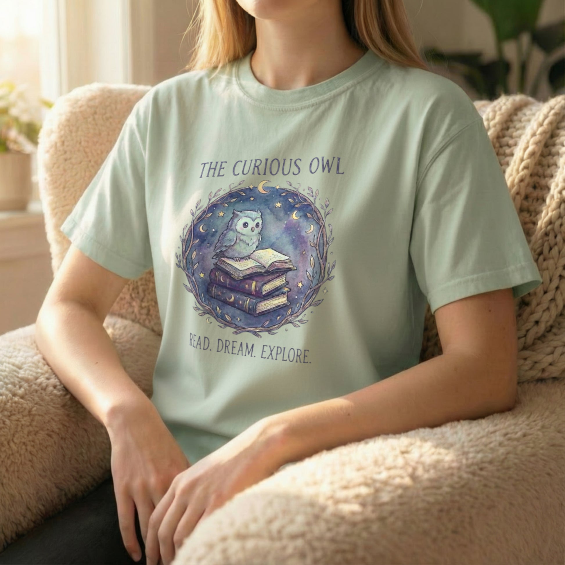 Lifestyle image of a model seated wearing the Curious Owl tee in sage, highlighting the soft watercolor owl artwork