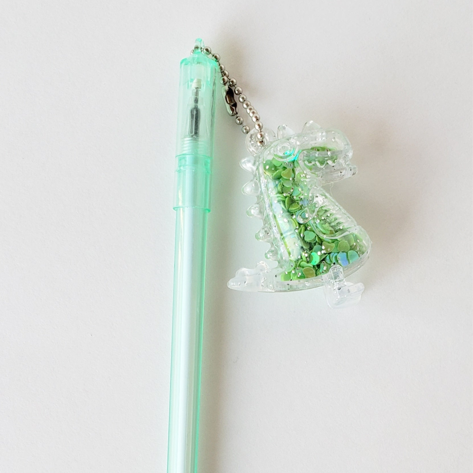 Closeup of the Dino Charm Gel Pen showing the detailed shaker dinosaur charm and ergonomic mint-green barrel grip against a white background