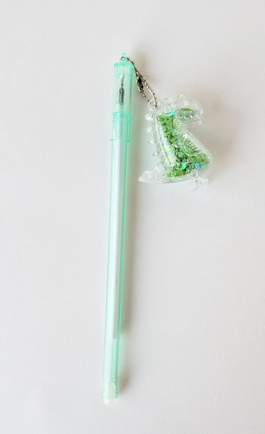 Flatlay of mint-green gel pen with attached silly dinosaur shaker charm on a white background