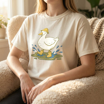 Woman sitting in a fuzzy armchair wearing an ivory t-shirt featuring a cute duck splashing in a puddle.