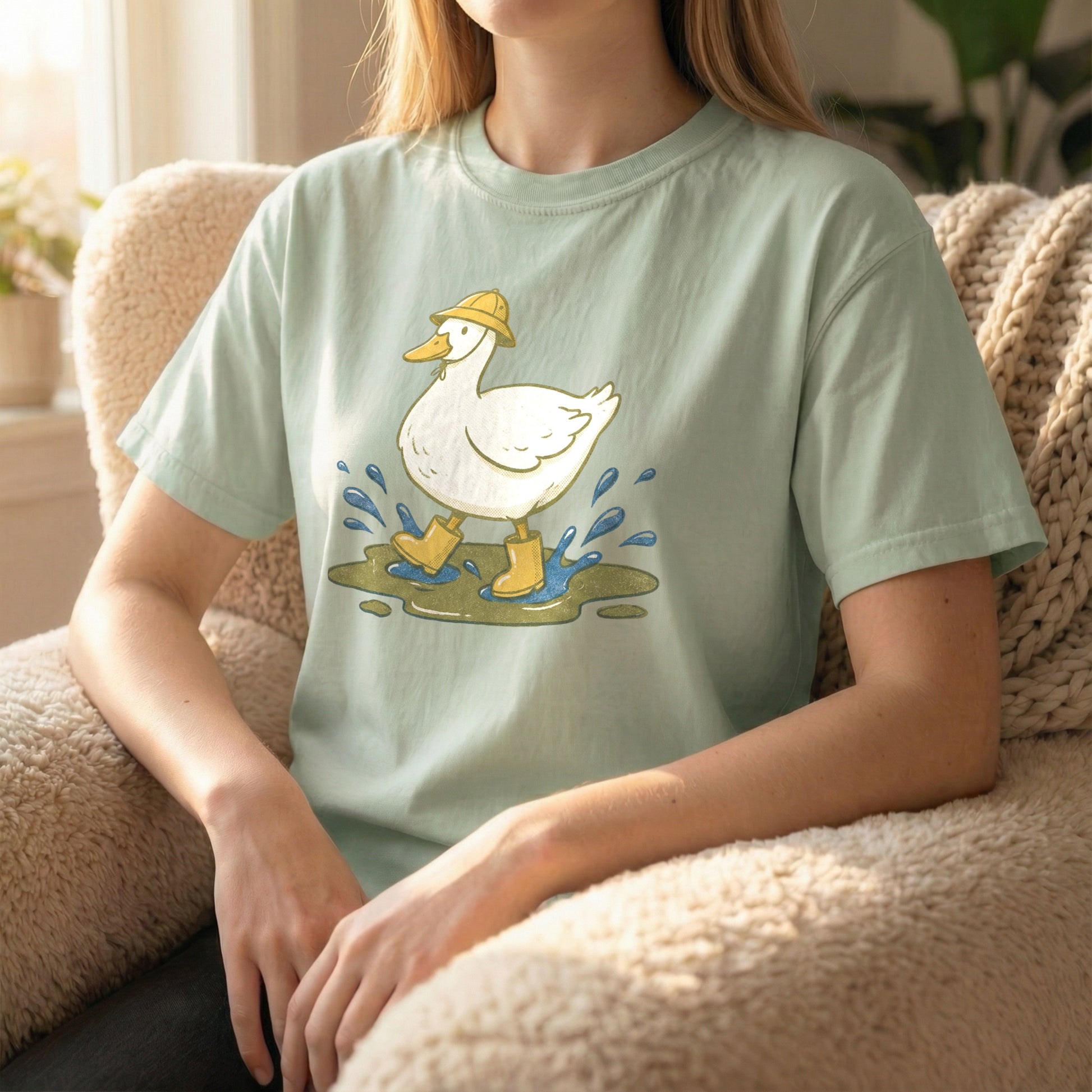 Woman sitting in a fuzzy armchair wearing a light green t-shirt featuring a cute duck splashing in a puddle.