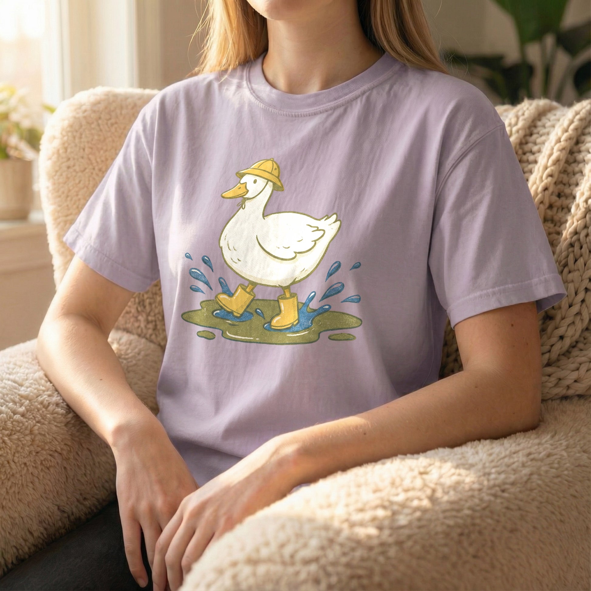 Woman sitting in a fuzzy armchair wearing an orchid purple t-shirt featuring a cute duck splashing in a puddle.