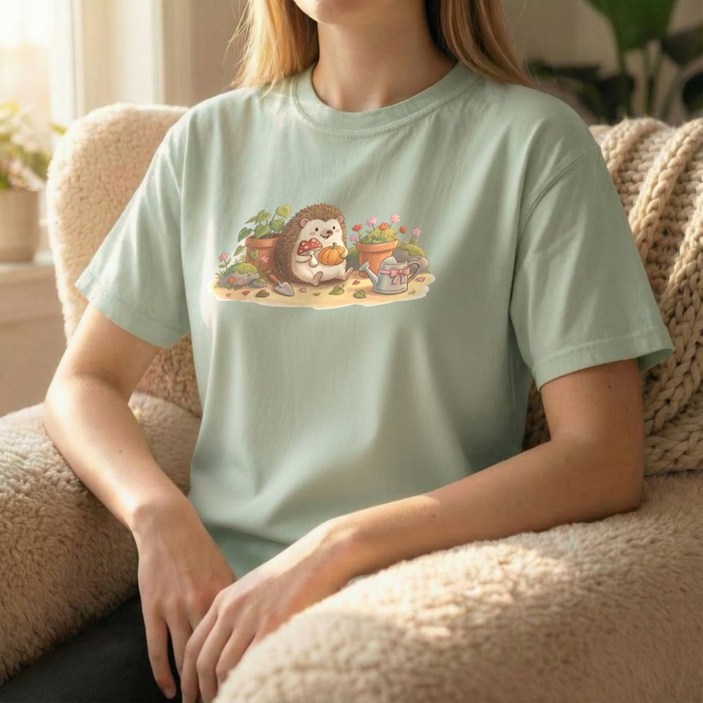 Garden Hedgehog tee worn sitting on couch on light green shirt with cheerful hedgehog garden scene