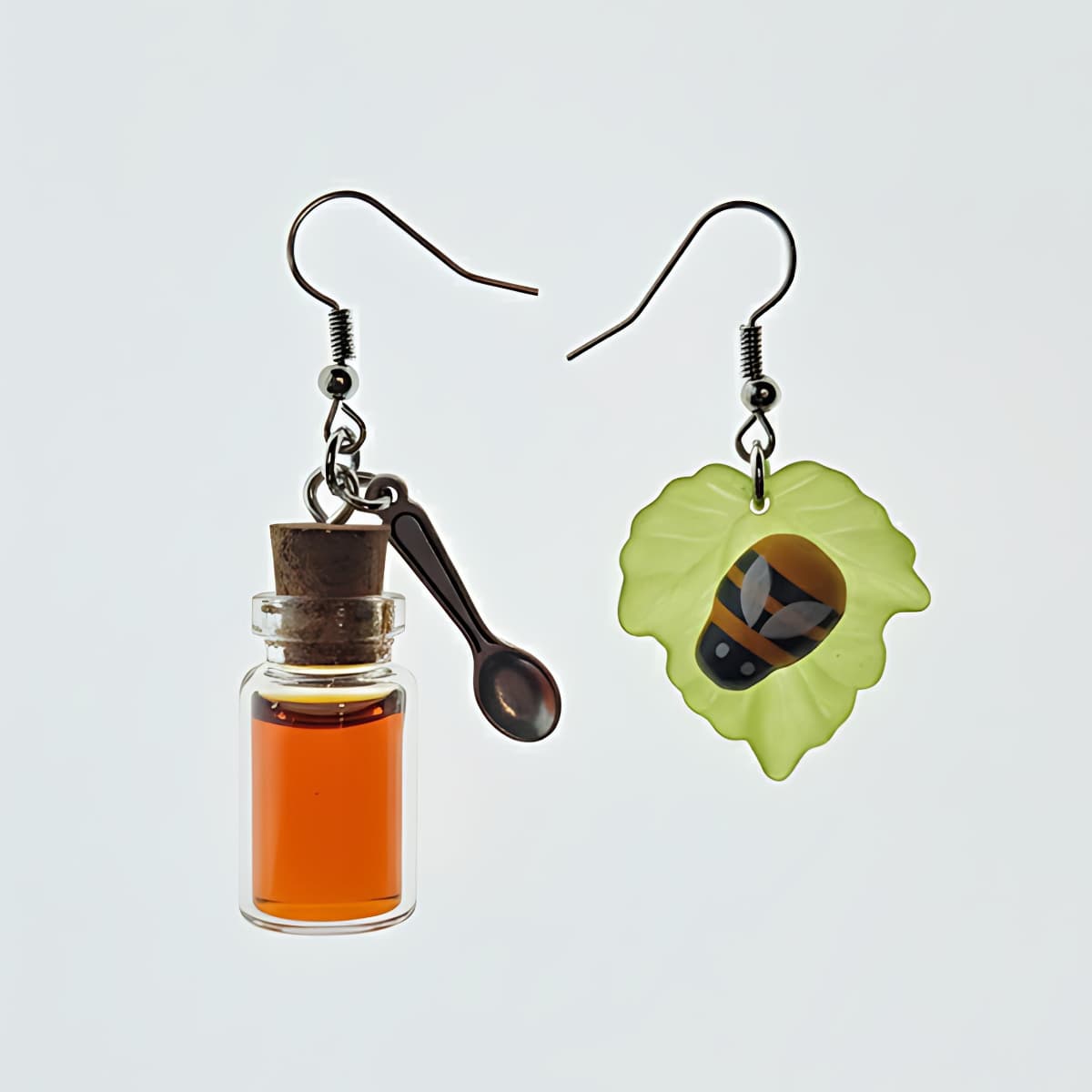 Mismatched honey jar and bee leaf earrings with spoon charm flatlay on white background