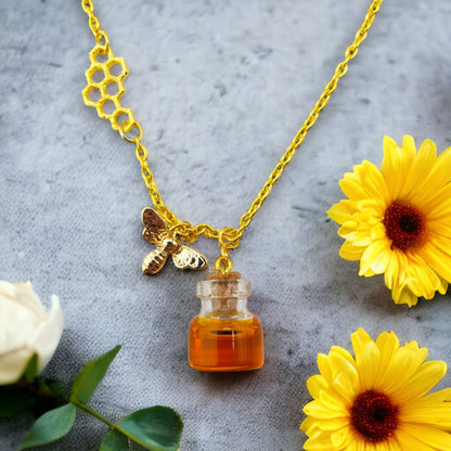 Honey jar necklace with golden bee charm and honeycomb design on gold chain, flowers shown as background only
