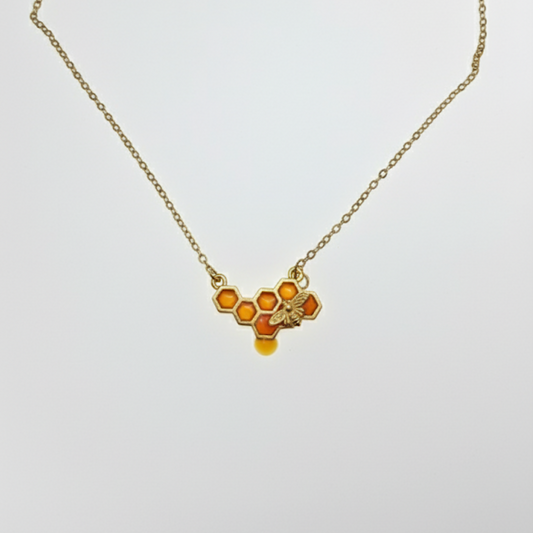 Honeycomb bee necklace with amber enamel detail on gold chain, white background