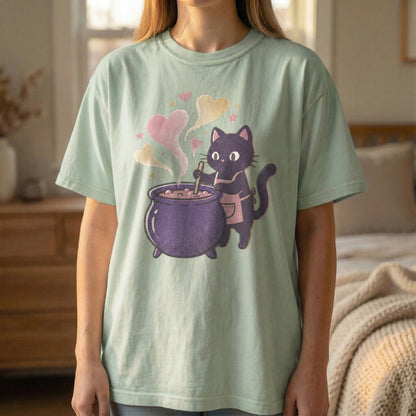 Mockup of a woman standing wearing a light green t-shirt with a pixel art black cat and purple cauldron design.