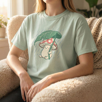 Woman sitting in a fuzzy armchair wearing a light green t-shirt with a cute mushroom and rain illustration.