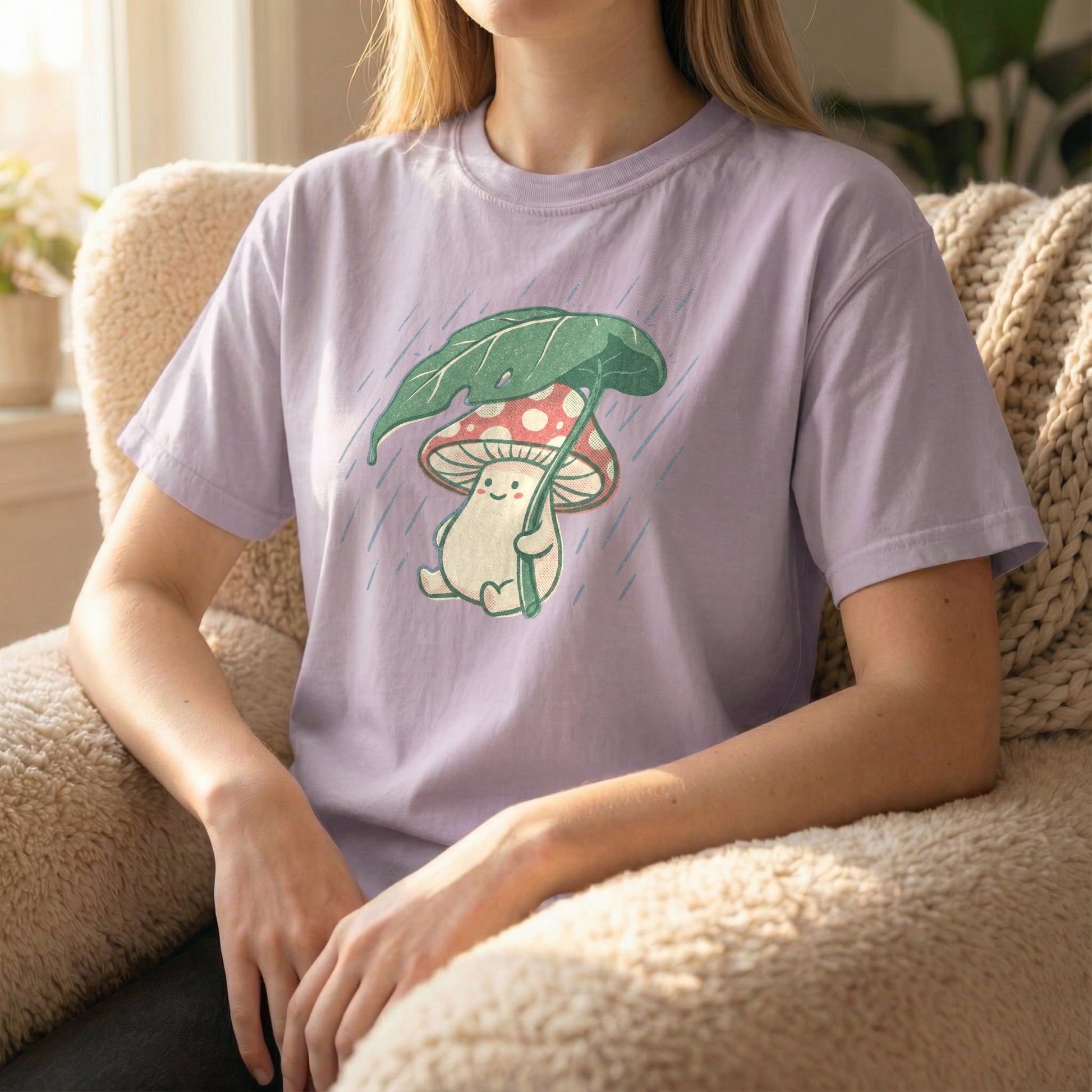 Woman sitting in a fuzzy armchair wearing an orchid purple t-shirt with a cute mushroom and rain illustration.
