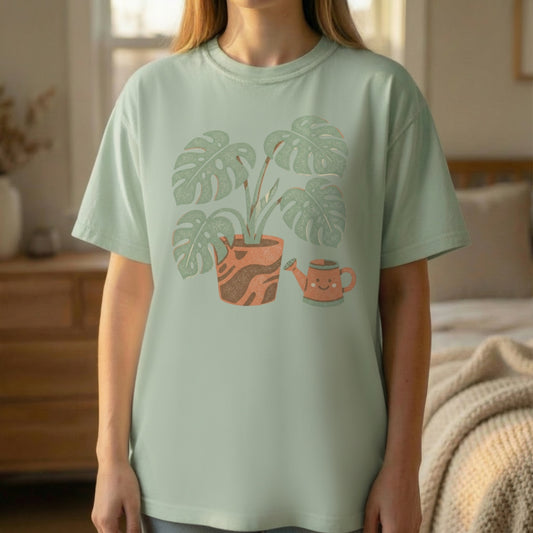 Woman wearing light green Plant Parent Tee featuring botanical monstera and watering can graphic