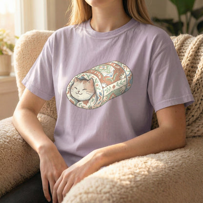 Model wearing an orchid Comfort Colors tee with a charming quilted cat burrito illustration while seated on a couch.