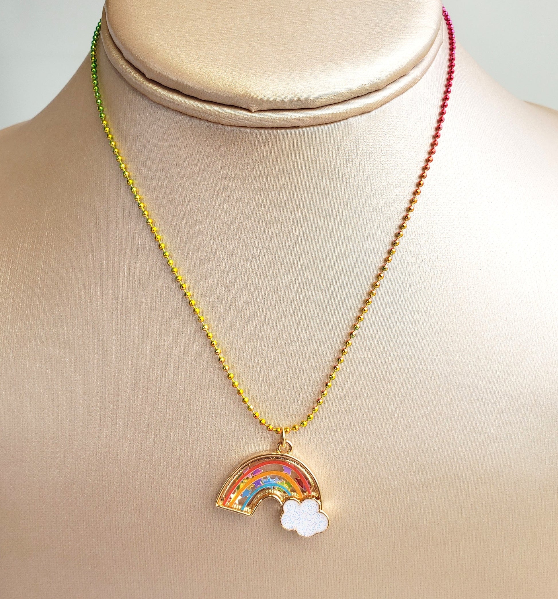 rainbow shaker necklace displayed on a beige jewelry bust showing the rainbow bead chain and confetti-filled pendant