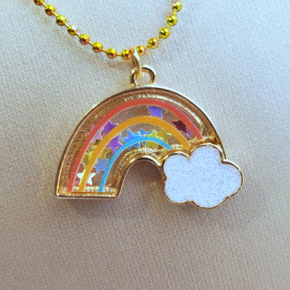 close-up of rainbow shaker necklace pendant filled with star confetti on a gold textured background