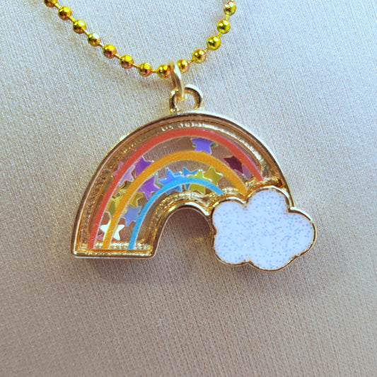 close-up of rainbow shaker necklace pendant filled with star confetti on a gold textured background