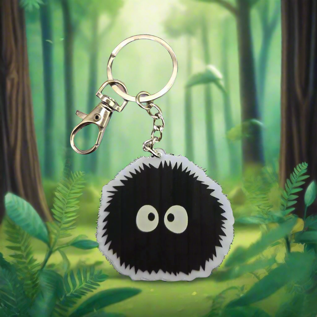 Soot Sprite acrylic keychain hanging in front of green forest background