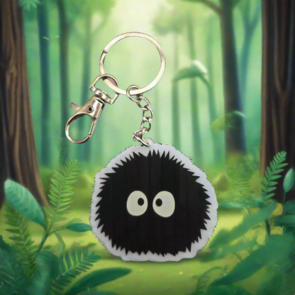 Soot Sprite acrylic keychain hanging in front of green forest background
