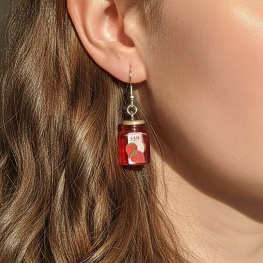 Close-up of strawberry jam jar dangle earring with glossy red detail worn on ear